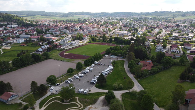 Der Wohnmobilstellplatz Wiesental in Münsingen im Biosphärengebiet Schwäbische Alb. Eine Luftaufnahme von einer Stadt. Im Vordergrund ist ein großer Sportplatz und ein Parkplatz mit mehreren Wohnmobilen.