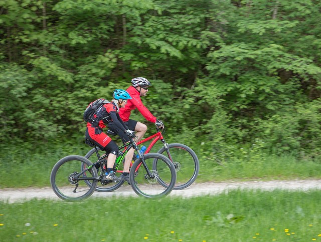 Radtouren in Münsingen im Biosphärengebiet Schwäbische Alb. Zwei Radfahrer*innen fahren auf einem Schotterweg.  Davor ist Wiese, dahinter ist Wald.