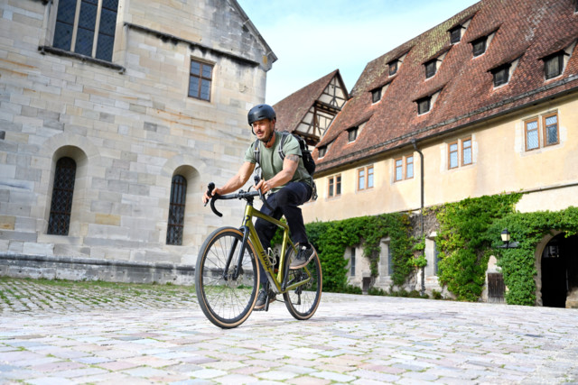 Die Gravel-Tour bei der Gea-Radserie rund um Münsingen im Biosphärengebiet Schwäbische Alb. Eine Person fährt in T-Shirt und Jeand auf einem Gravelbike durch eine historische Altstadt.