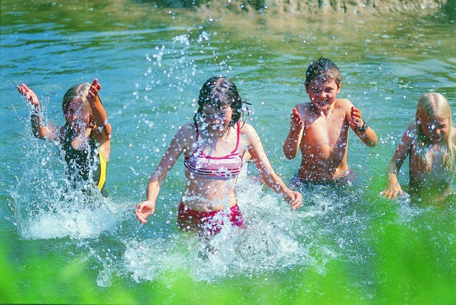 Baden in der Lauter im Großen Lautertal in Münsingen im Biosphärengebiet Schwäbische Alb. Vier Kinder baden in einem natürlichen Gewässer und spritzen mit Wasser um sich. Dabei verziehen sie ihre Gesichter.
