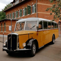 Das Oldtimerfest am Eisberg im Stadtteil Dottingen im Münsingen im Biosphärengebiet Schwäbische Alb. Ein gelber Oldtimer-Bus steht vor einem historischen Backsteingebäude.