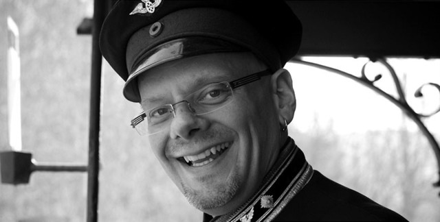 Bernd Weckler ist ein Münsinger Original mit seiner Schwäbischen Alb-Bahn in Münsingen im Biosphärengebiet Schwäbische Alb. Ein schwarz weiß Bild einer Person in Uniform, einer Mütze und einer Brille lächelt in die Kamera.