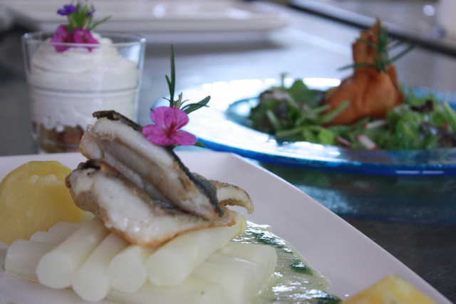 Schwäbische Kulinarik im Land- und Ferienhotel Wittstaig im Großen Lautertal in Münsingen im Biosphärengebiet Schwäbische Alb. Auf einem Tisch stehen ein Teller mit Spargel, Fisch und Kartoffeln. Im Hintergrund ein Teller mit Salat und Glas mit Nachttisch.