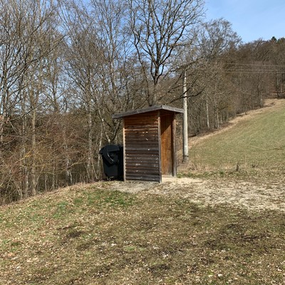 Zeltplatz Stettener Häule im Großen Lautertal in Münsingen im Biosphärengebiet Schwäbische Alb. Eine Wiese mit einer kleinen Holzhütte hinter der ein Mülleimer steht.