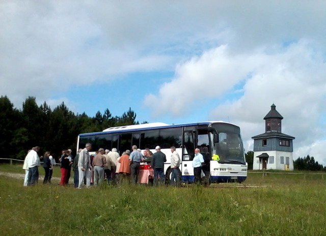 TrÜP-Touren mit dem Bus auf dem ehemaligen Truppenübungsplatz  in Münsingen im Biosphärengebiet Schwäbsiche Alb. Eine Gruppe von Menschen steht vor einem Reisebus, im Hintergrund ist ein Turm mit blauer Holzvertäfelung.
