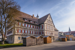 Das Rathaus in der Innenstadt von Münsingen im Biosphärengebiet Schwäbische Alb. Ein großes Gebäude mit einer Fachwerkfassade und einer großen Uhr. Davor stehen auf einem Platz mehrere Holzhütten.