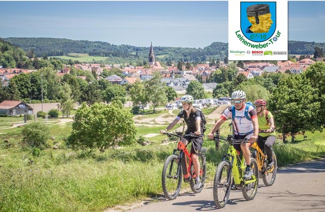 Die Leinenweber-Tour führt von Münsingen zu BeckaBeck´ s H-Albzeit nach Merklingen im Biosphärengebiet Schwäbische Alb. Drei Radfahrer*innen fahren mit E-Bikes in kurzen Radklamotten versetzt auf einem Teerweg. Im Hintergrund ist eine Stadt, ein Bikepark und vereinzelt Wohnmobile.